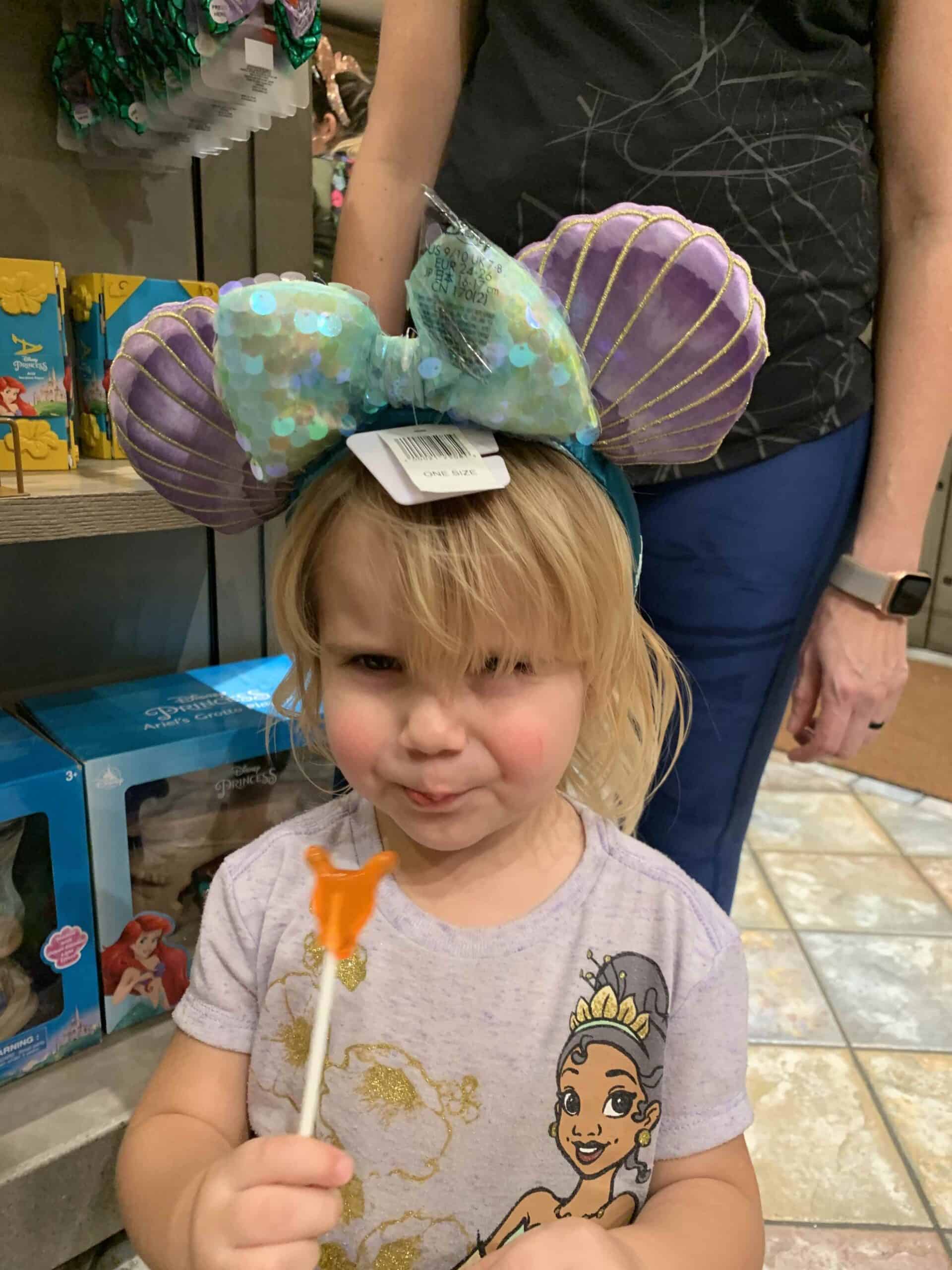 blonde toddler girl with purple mickey ears and butterfly lollipop
